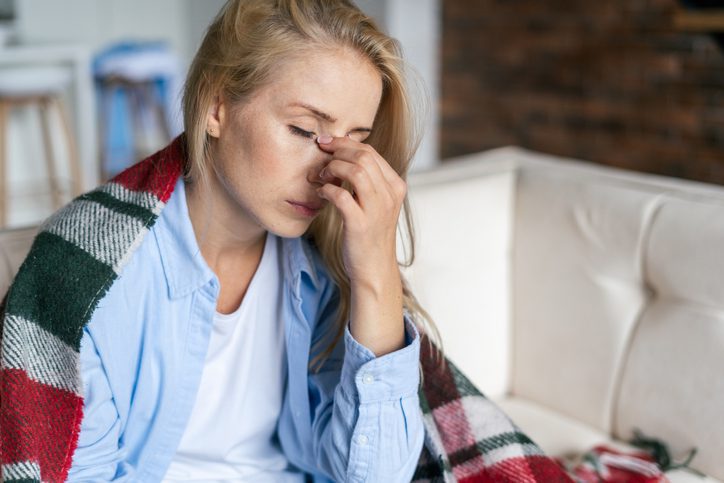 Woman, sick with the flu, with closed eyes holding her nose.
